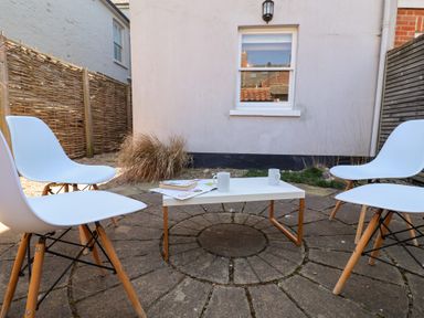 An outdoor patio area with a white table and four white chairs on a circular stone floor at Kestrel in Southwold
