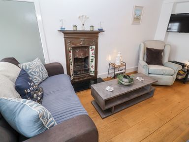 A living room with a sofa, armchair, coffee table, fireplace and wall-mounted TV at Dolphin Cottage Southwold