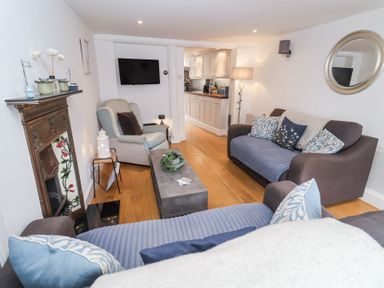A living room with two sofas a armchair a coffee table and a wall-mounted television at Dolphin Cottage in Southwold