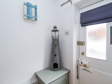 A corner of a room with a white door featuring a blue blind and a decorative lighthouse on a green cabinet at Dolphin Cottage Southwold
