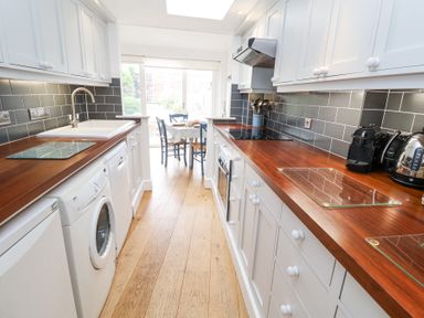 A kitchen with wooden countertops white cabinets and appliances leading to a dining area at Dolphin Cottage Southwold