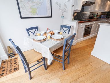 A kitchen dining area with a table set for four people with plates glasses of orange juice and croissants at Dolphin Cottage Southwold