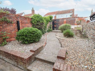 A garden area with a brick and stone pathway surrounded by gravel beds and bushes at Dolphin Cottage Southwold