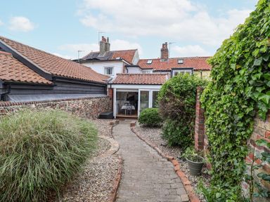 A garden pathway with bushes on either side leading to a house with tiled roofs at Dolphin Cottage Southwold