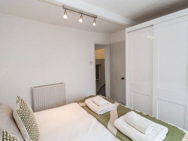 A bedroom with a bed with folded towels and pillows beside a white sliding door wardrobe at Dolphin Cottage Southwold