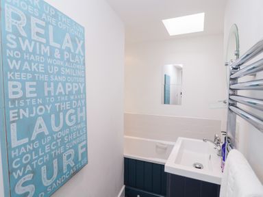 A bathroom with a bathtub a sink a towel rack and a blue wall sign with text at Dolphin Cottage Southwold