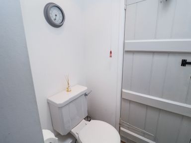 A small bathroom with a white toilet a clock on the wall and a white wooden door at Dolphin Cottage Southwold