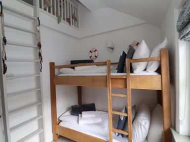 A small bedroom with wooden bunk beds pillows towels and a white ladder at Dolphin Cottage Southwold