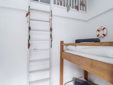A wooden bunk bed with folded blankets and a white ladder decorated with small fish ornaments in a white room at Dolphin Cottage Southwold