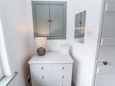 A white dresser with a lamp and small white cabinet on top below a closed cabinet and two mirrors on the wall at Dolphin Cottage Southwold