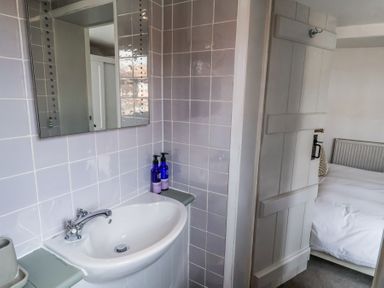 A bathroom sink with a mirror and soap dispensers next to a partially open door showing a bedroom at Dolphin Cottage Southwold