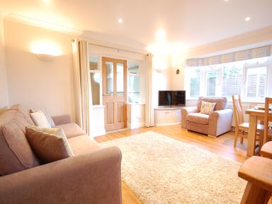 A living room with two sofas a television on a cabinet a dining table and chairs and a door with windows at Garden Cottage Southwold
