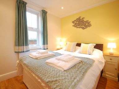 A bedroom with a double bed two bedside tables with lamps and a window with curtains at Garden Cottage Southwold