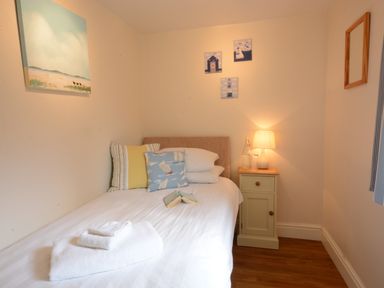 A bedroom with a single bed pillows a bedside table with a lamp and wall paintings at Garden Cottage Southwold