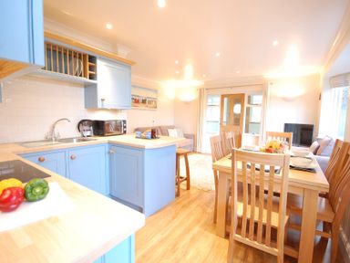 An open kitchen and dining area with blue cabinets and a wooden dining table at Garden Cottage Southwold