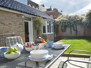 A patio table set with bowls fruit and cups in a garden next to a brick house at Garden Cottage Southwold