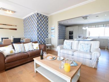 A living room with two sofas a wooden coffee table and a dining area with oars on the wall at St Marys View Southwold