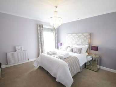A bedroom with a double bed bedside tables with lamps curtains and a chandelier at St Marys View Southwold