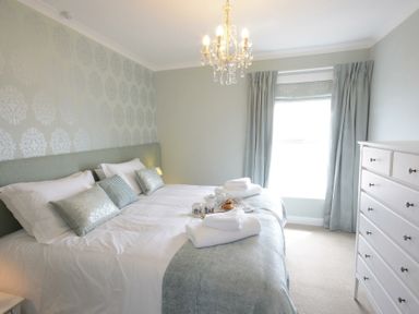 A bedroom with a double bed chest of drawers and a window with curtains at St Marys View Southwold