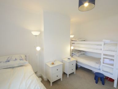 A bedroom with a single bed a bunk bed two white bedside tables and a floor lamp at St Marys View Southwold