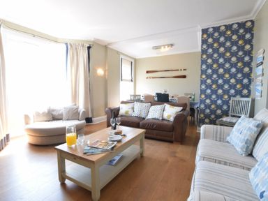 A living room with sofas a coffee table and dining table with paddle decorations on the wall at St Marys View Southwold