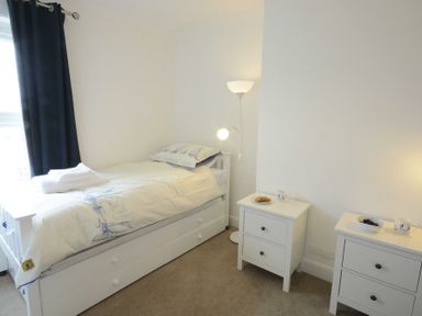 A bedroom with a single bed next to two white bedside tables with lamps and cups at St Marys View Southwold