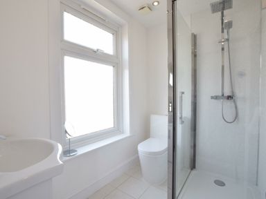 A bathroom with a sink a toilet a shower with glass door and a window at St Marys View Southwold