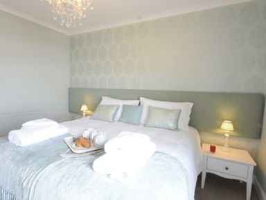 A bedroom with a double bed white bedding nightstands lamps and a tray with breakfast at St Marys View Southwold
