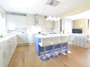 A kitchen with white cabinets a blue island and four white bar stools at St Marys View Southwold
