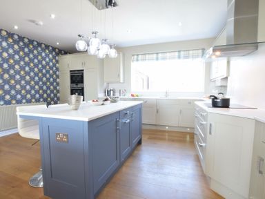 A kitchen with a blue island, white chairs, patterned wallpaper, and large window at St Marys View, Southwold