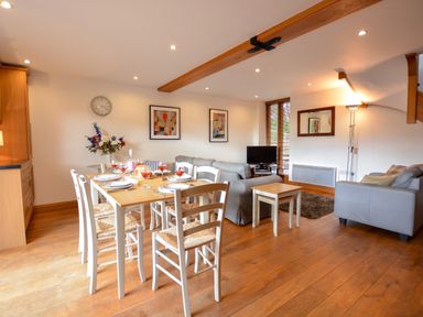 A dining area with a table set for six and a living area with two sofas and a TV at Three Chantry Barns Orford