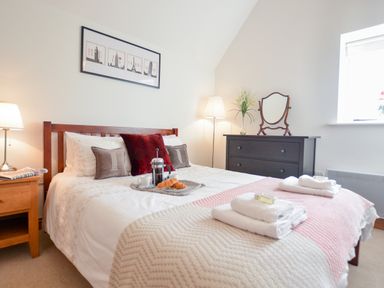 A bedroom with a bed with pillows and a tray with breakfast items next to a wooden nightstand and a dark dresser with a mirror at Three Chantry Barns in Orford