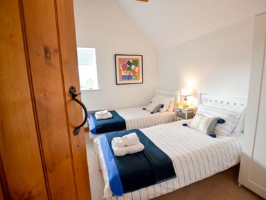 A bedroom with two single beds with striped bedding a bedside table with a lamp and orange juice and a colorful framed picture on the wall at Three Chantry Barns Orford