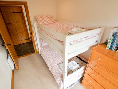 A small bedroom with a white bunk bed and wooden chest of drawers with books at Three Chantry Barns Orford
