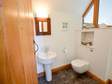 A bathroom with a pedestal sink mirror wall light toilet and shelf with decorations at Three Chantry Barns Orford