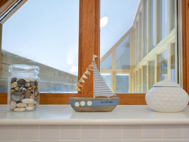 A windowsill with a jar of pebbles a decorative sailboat and a white ceramic container at Three Chantry Barns Orford