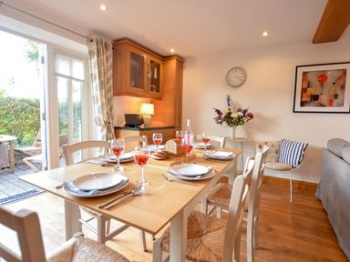 A dining area with a wooden table set for six near a glass door leading outside at Three Chantry Barns Orford