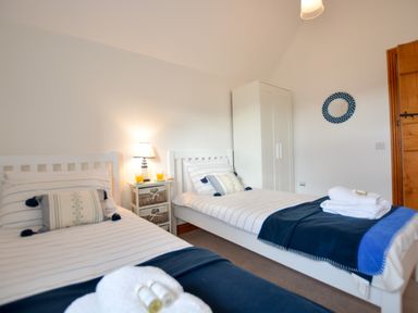 A bedroom with two single beds with striped bedding a bedside table with a lamp and drinks a white wardrobe and a round mirror on the wall at Three Chantry Barns Orford