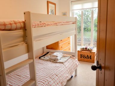 A bedroom with bunk beds a wicker basket a chest of drawers and a window with blinds at Three Chantry Barns Orford