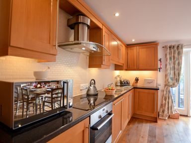A kitchen with wooden cabinets a black countertop microwave and a kettle at Three Chantry Barns Orford