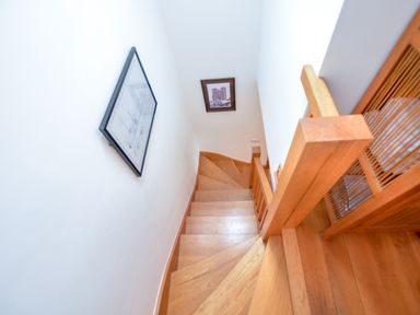 A wooden staircase with handrails and framed pictures on white walls at Three Chantry Barns in Orford