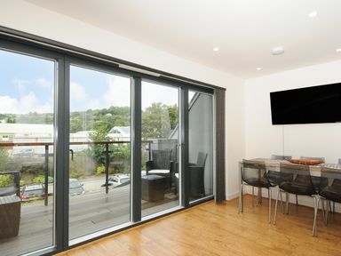 A dining area with a glass table and black chairs next to large sliding glass doors opening to a balcony at Bluebell Retreat in Lostwithiel