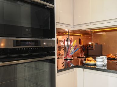 A kitchen corner with a built in oven, a knife holder with colorful knives, plates with croissants and a striped mug at Bluebell Retreat in Lostwithiel