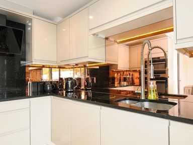 A kitchen with black countertops white cabinets a stainless steel faucet and appliances at Bluebell Retreat in Lostwithiel