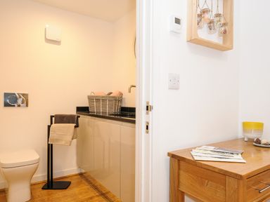 A bathroom with a toilet and cabinet with towels and a wooden table with books at Bluebell Retreat in Lostwithiel