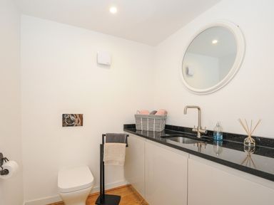 A bathroom with a toilet, sink, round mirror, towels, and a countertop at Bluebell Retreat in Lostwithiel