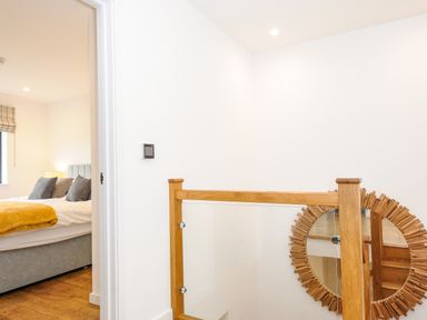 A hallway with a wooden and glass stair railing and a round mirror on the wall next to a bedroom at Bluebell Retreat in Lostwithiel