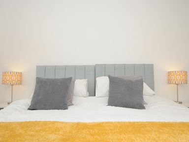 A bedroom with a bed having gray headboards gray pillows white bedding and a yellow throw at Bluebell Retreat in Lostwithiel