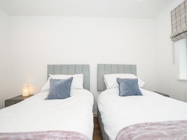 A bedroom with two single beds each with a blue pillow and white bedding at Bluebell Retreat in Lostwithiel