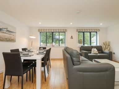 A dining area with a table set for six and a living area with two gray sofas and windows at Bluebell Retreat in Lostwithiel
